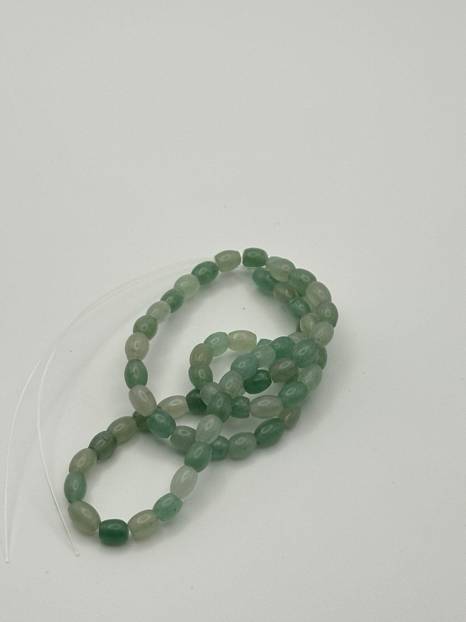 A string of light green oval rice puffed aventurine beads on a white surface