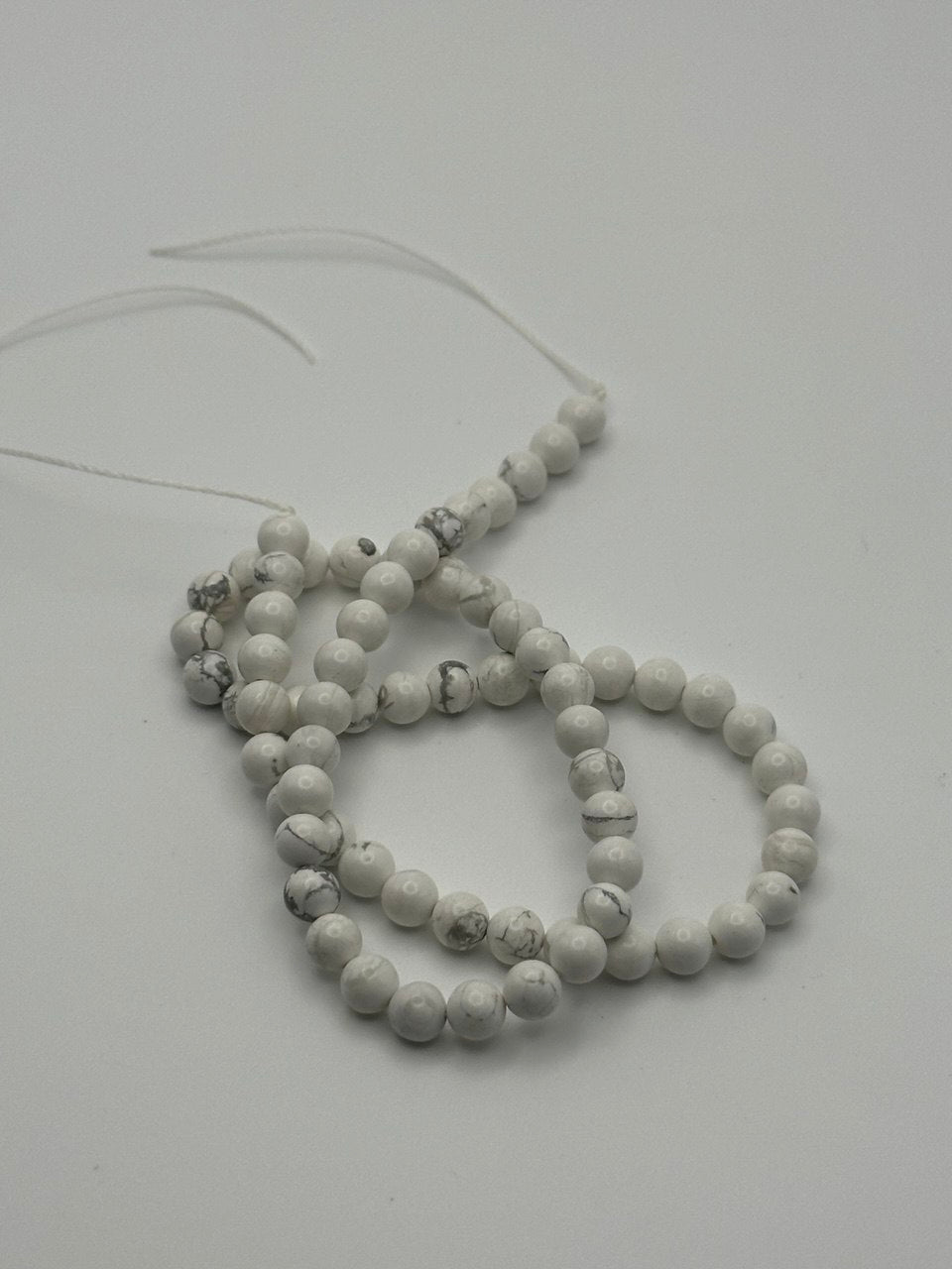 A string of white magnesite round beads on a white surface