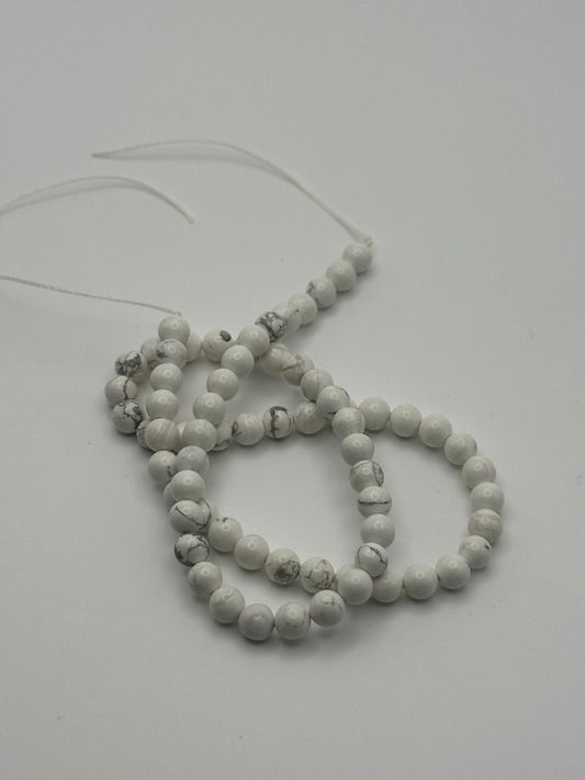 A string of white magnesite round beads on a white surface