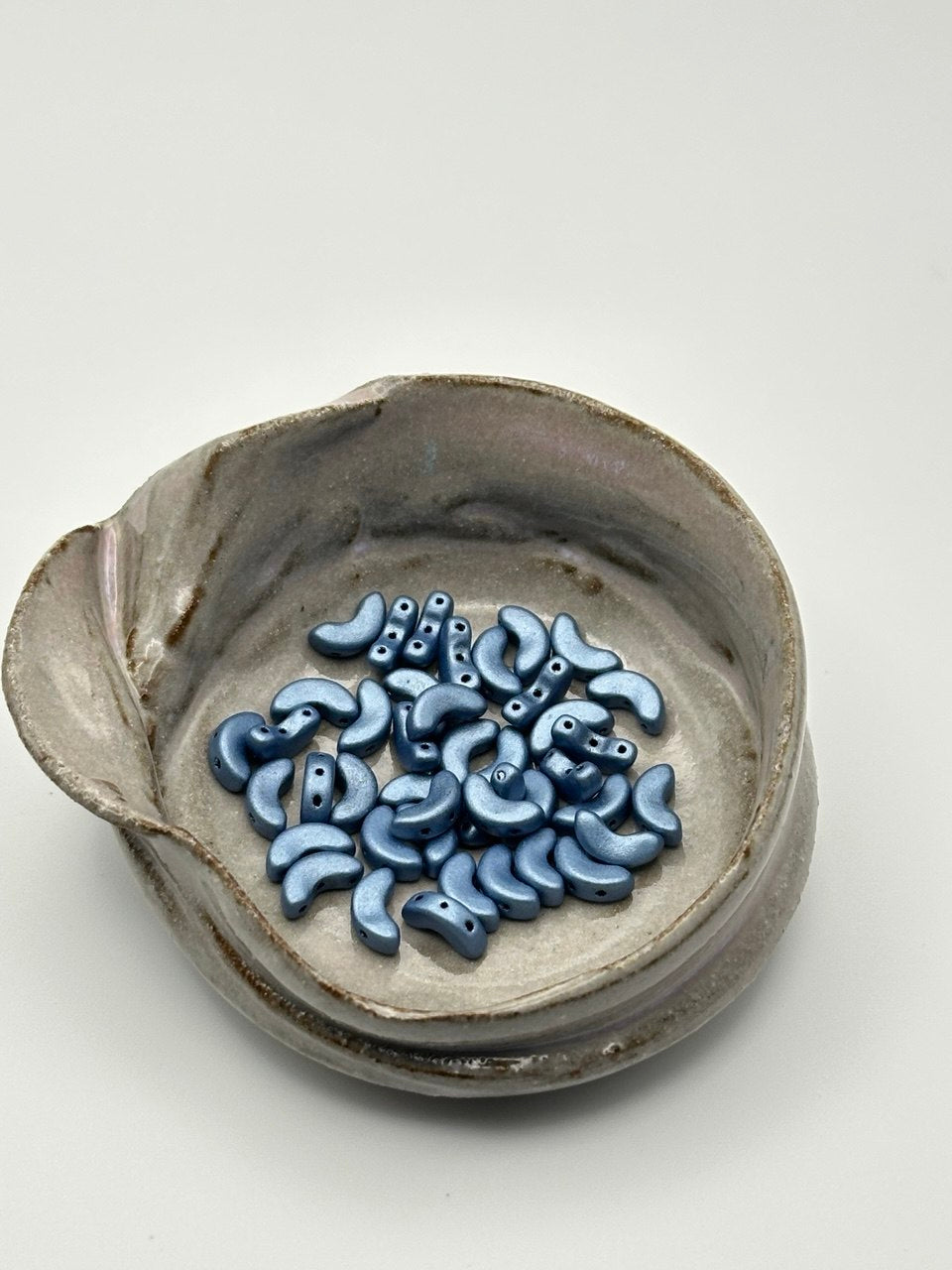 Ceramic dish with metallic matte blue arcos par puca beads on a white background