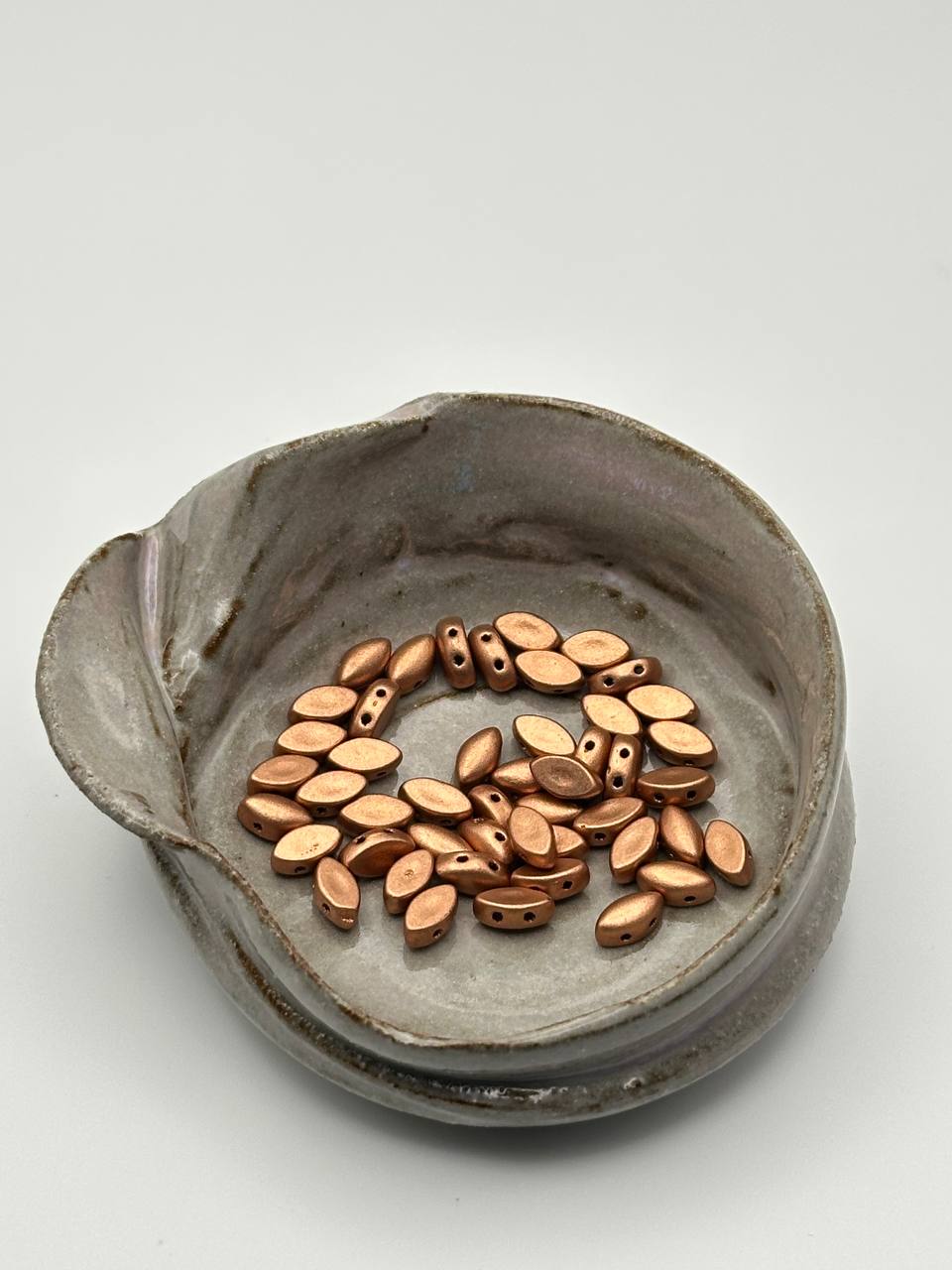 A ceramic dish with irisduo vintage copper beads on a white surface