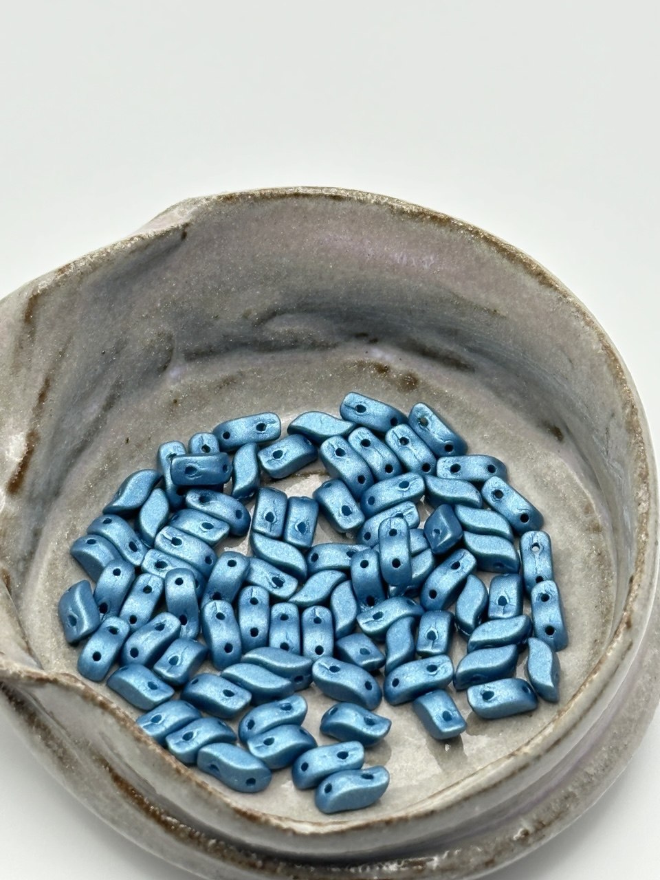 Blue ceramic beads in a gray pot on a white background