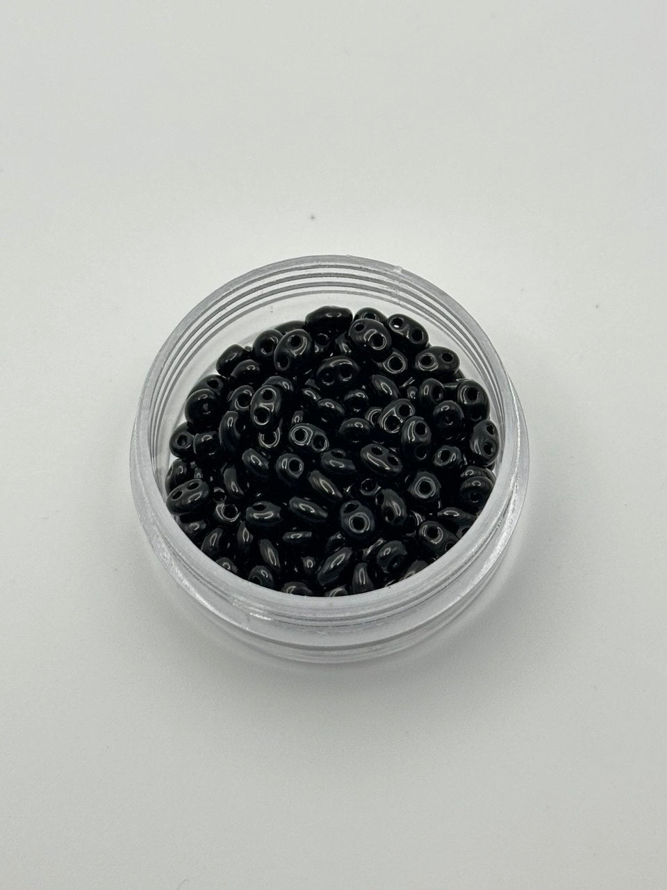 Small clear container filled with black beads on a light gray background