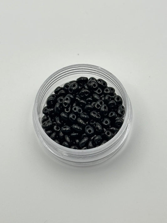 Small clear container filled with black beads on a light gray background