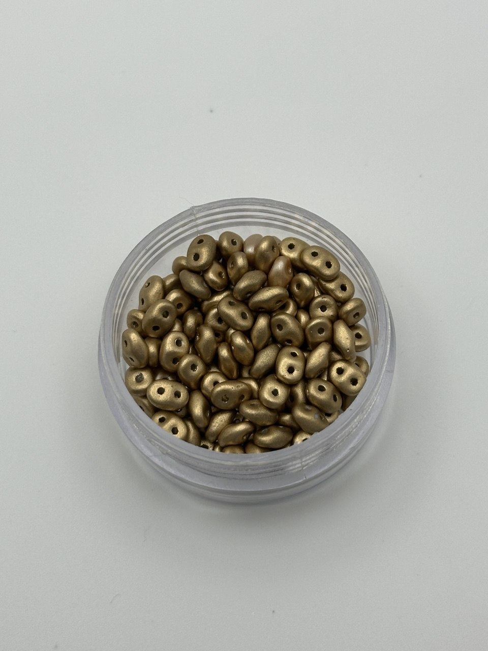 Small container filled with metallic gold beads on a light gray background