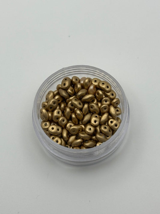 Small container filled with metallic gold beads on a light gray background