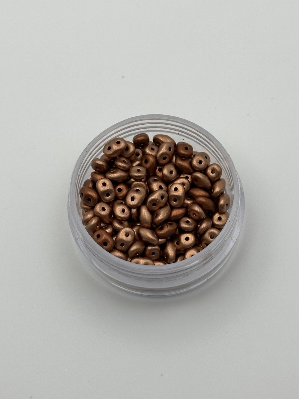 Clear container filled with small metallic beads on a light gray background