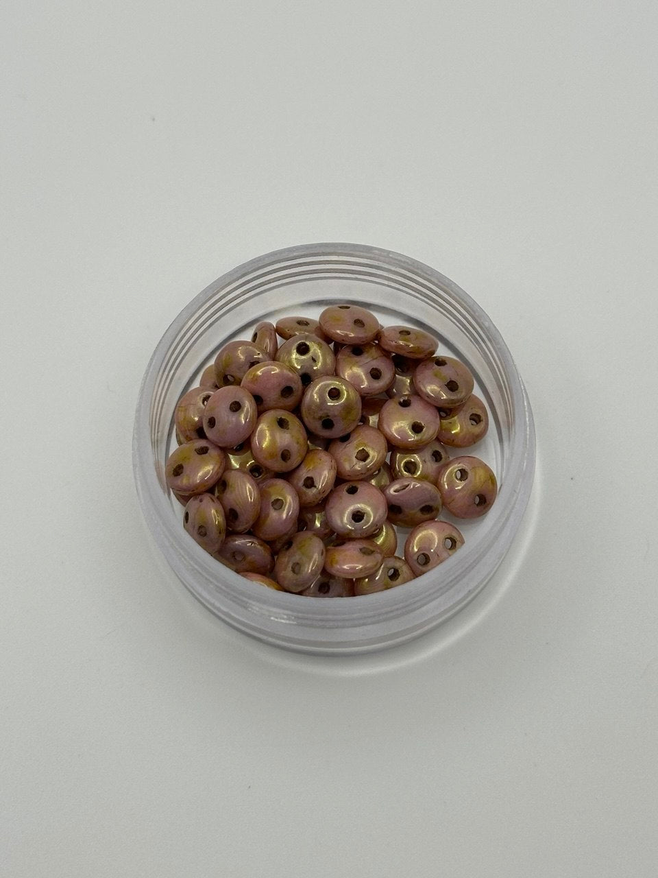 Small clear container filled with round 2-hole rose gold beads on a white background