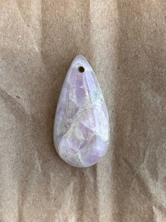 A teardrop-shaped gemstone pendant with a small hole at the top, resting on a textured brown paper background.