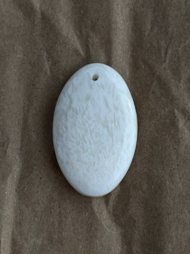 An oval white stone pendant with a small hole at the top, resting on a brown textured paper background.