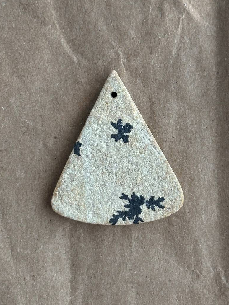 A triangular druzy pendant with a small hole at the top, featuring a dark blue snowflake pattern on a textured off-white glaze, displayed on a brown kraft paper background.