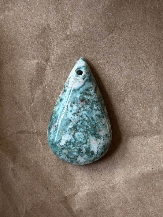 A smooth teardrop tree agate cabochon on brown paper background