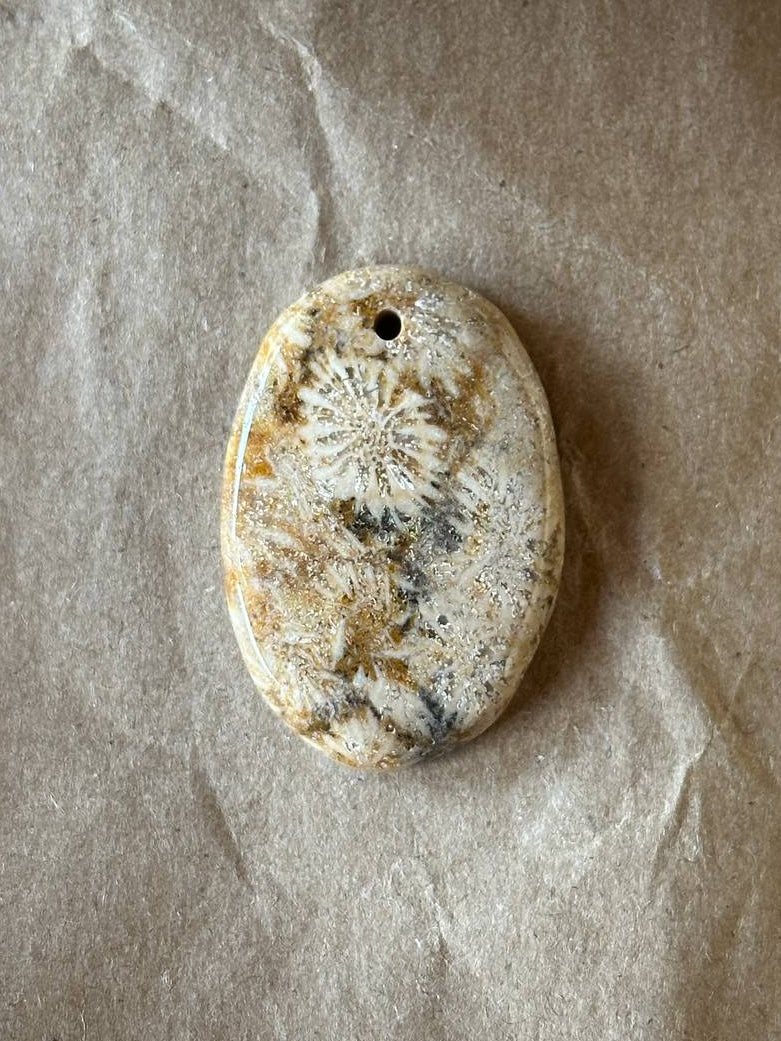 An oval stone pendant featuring a detailed sea urchin or starfish fossil pattern, resting on a textured sheet of brown paper.