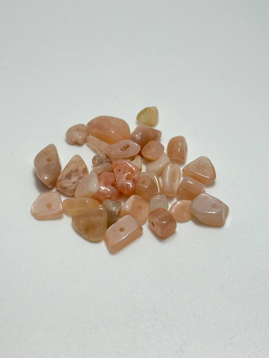 A small pile of apricot agate irregular chip beads on white background