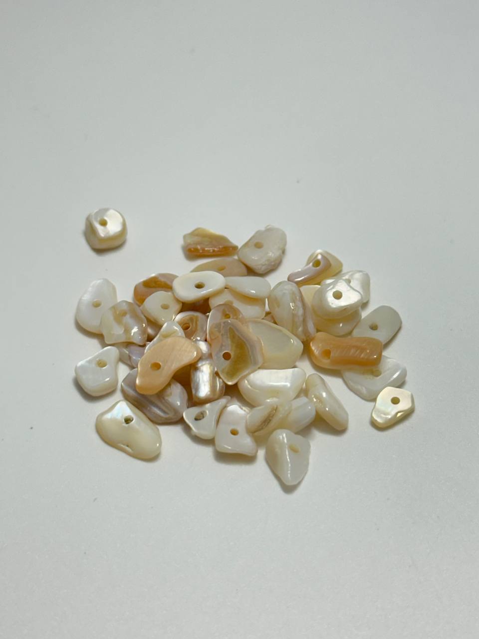 A small pile of mother of pearl chip beads on white background