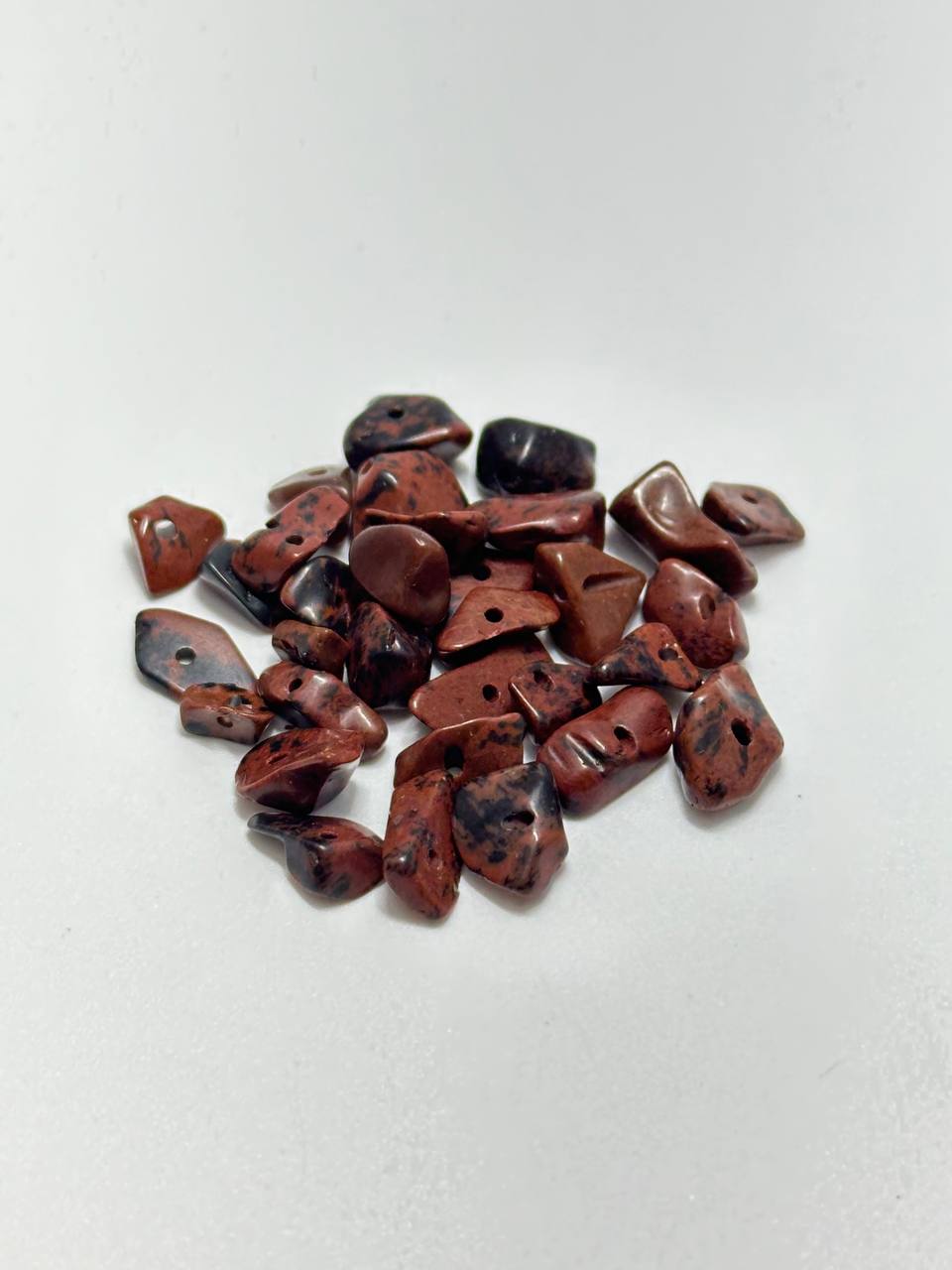 A small pile of mahogany obsidian chip beads on white background