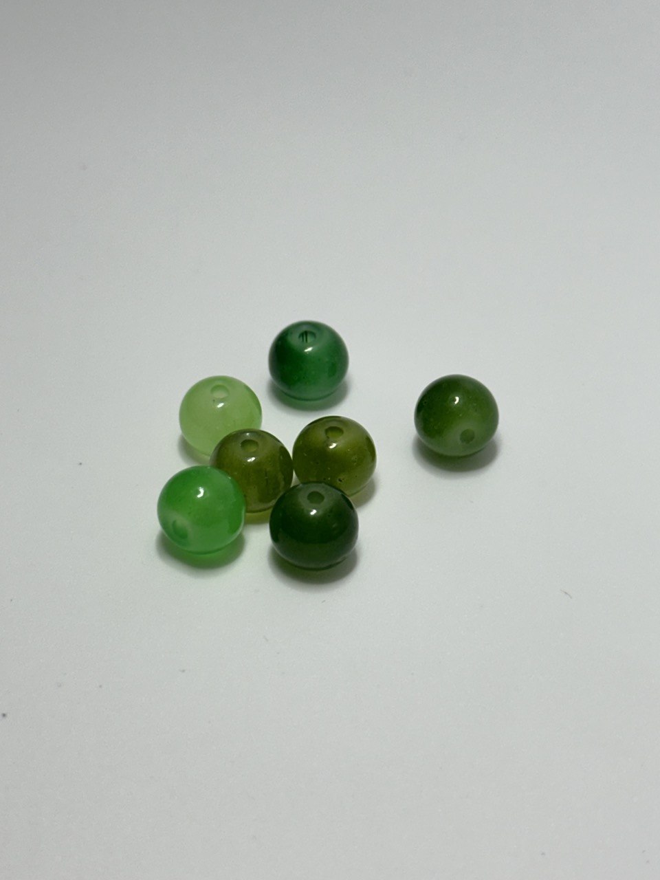 Seven green painted glass beads on white surface