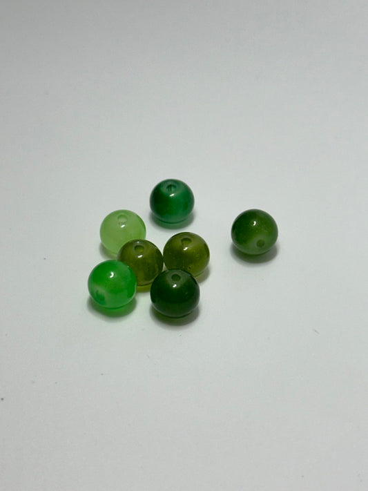 Seven green painted glass beads on white surface