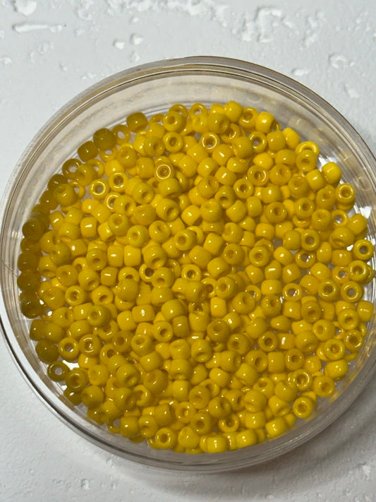Yellow seed beads in a clear round container on a light textured background.