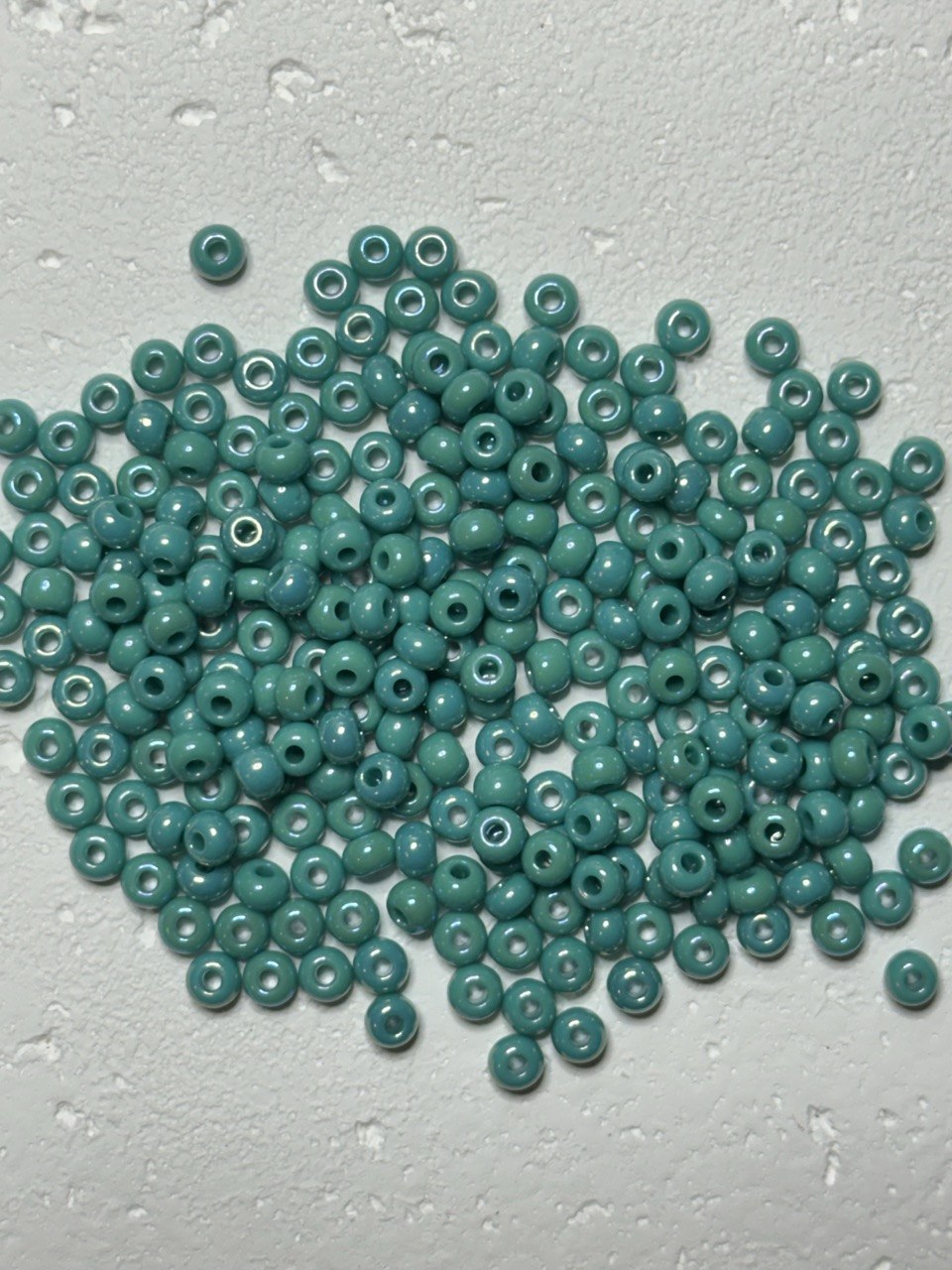 A pile of small round turquoise beads with white centers, scattered on a textured light gray surface.