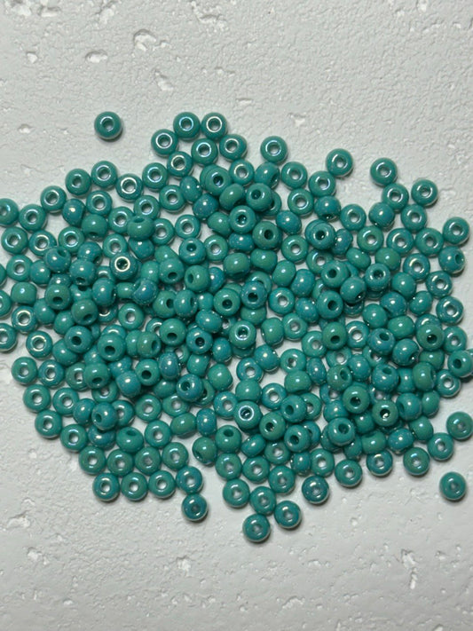 A pile of small round turquoise beads with white centers, scattered on a textured light gray surface.