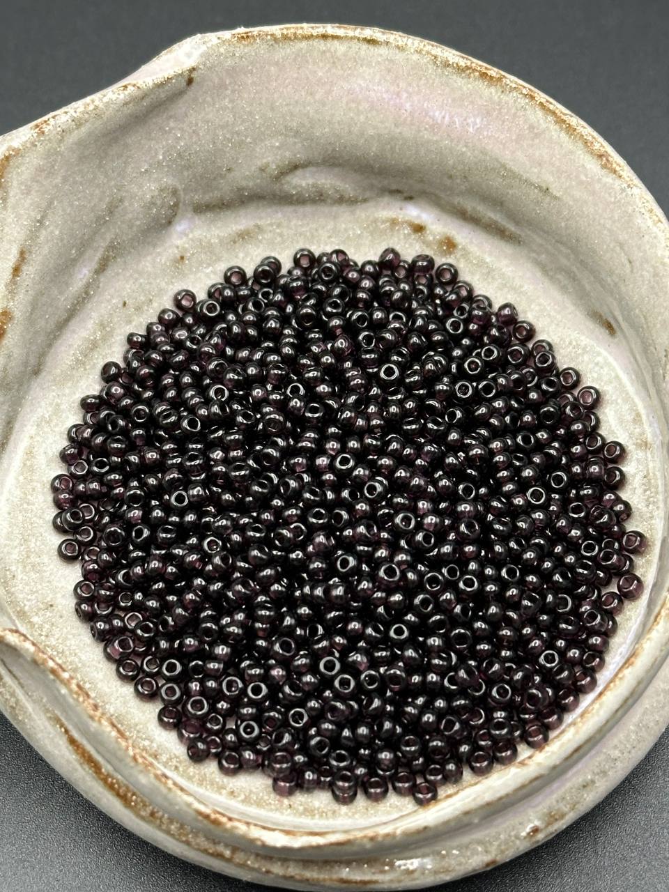 Small container filled with dark violet beads on a gray background