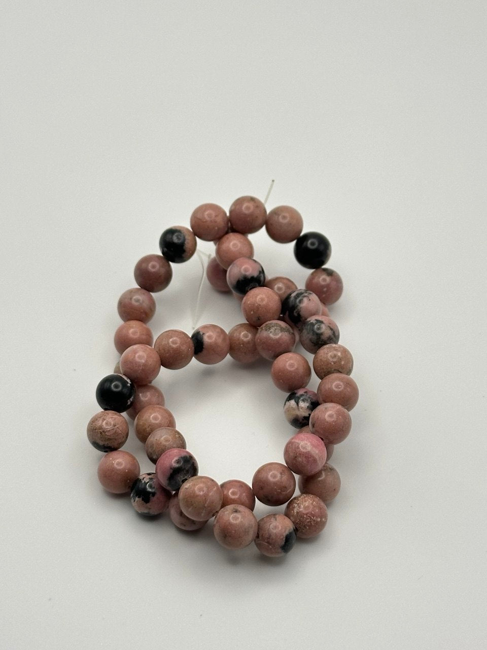 A string of pink rhodonite round smooth beads with black inclusions on a white surface