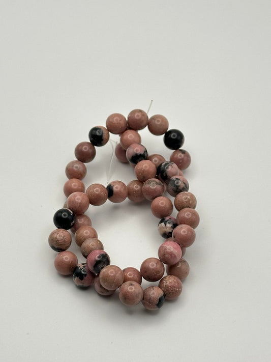 A string of pink rhodonite round smooth beads with black inclusions on a white surface