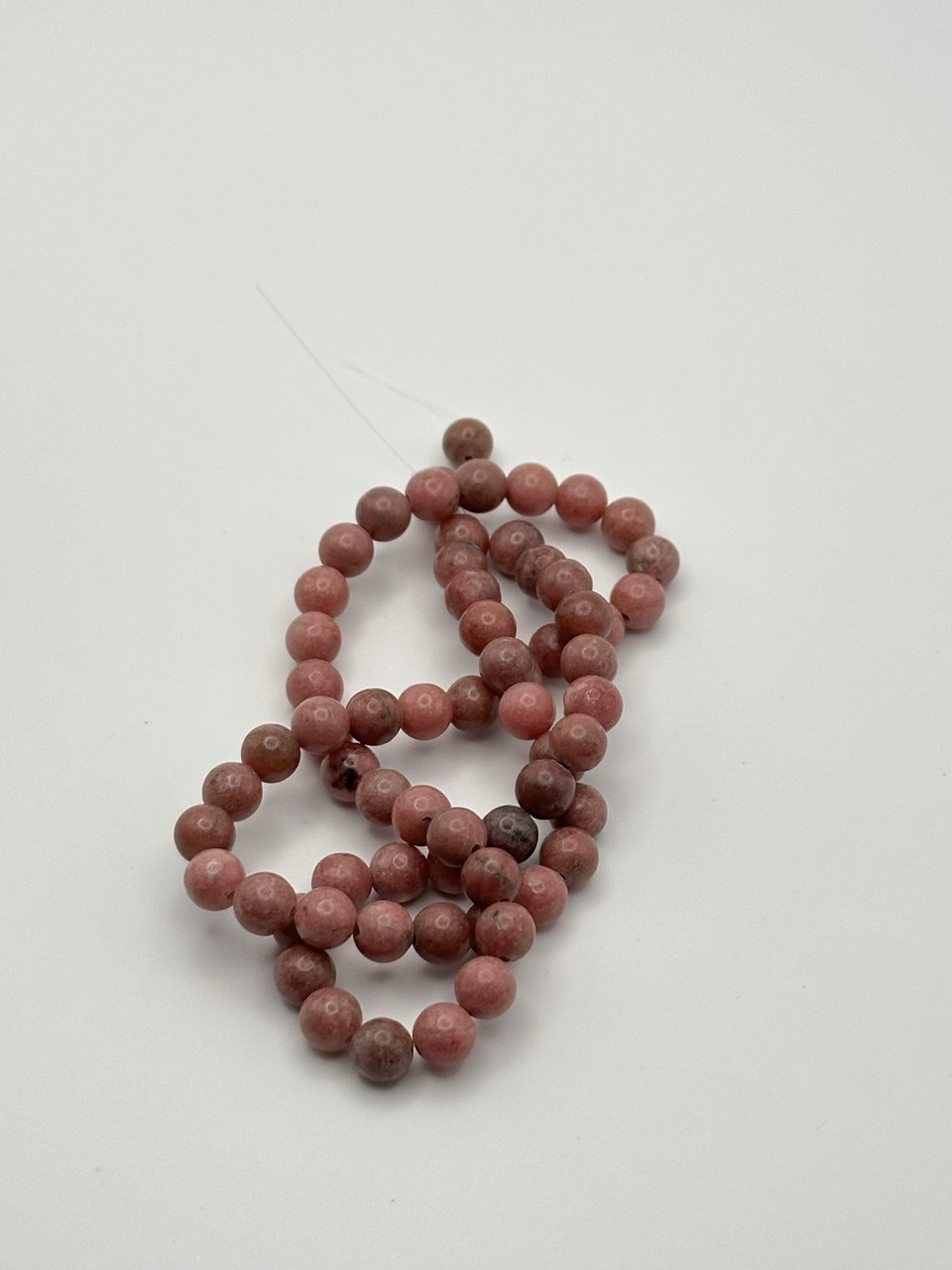 A string of dusty dark pink rhodonite round beads on a white surface
