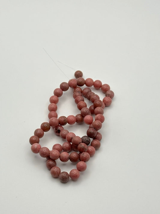 A string of dusty dark pink rhodonite round beads on a white surface