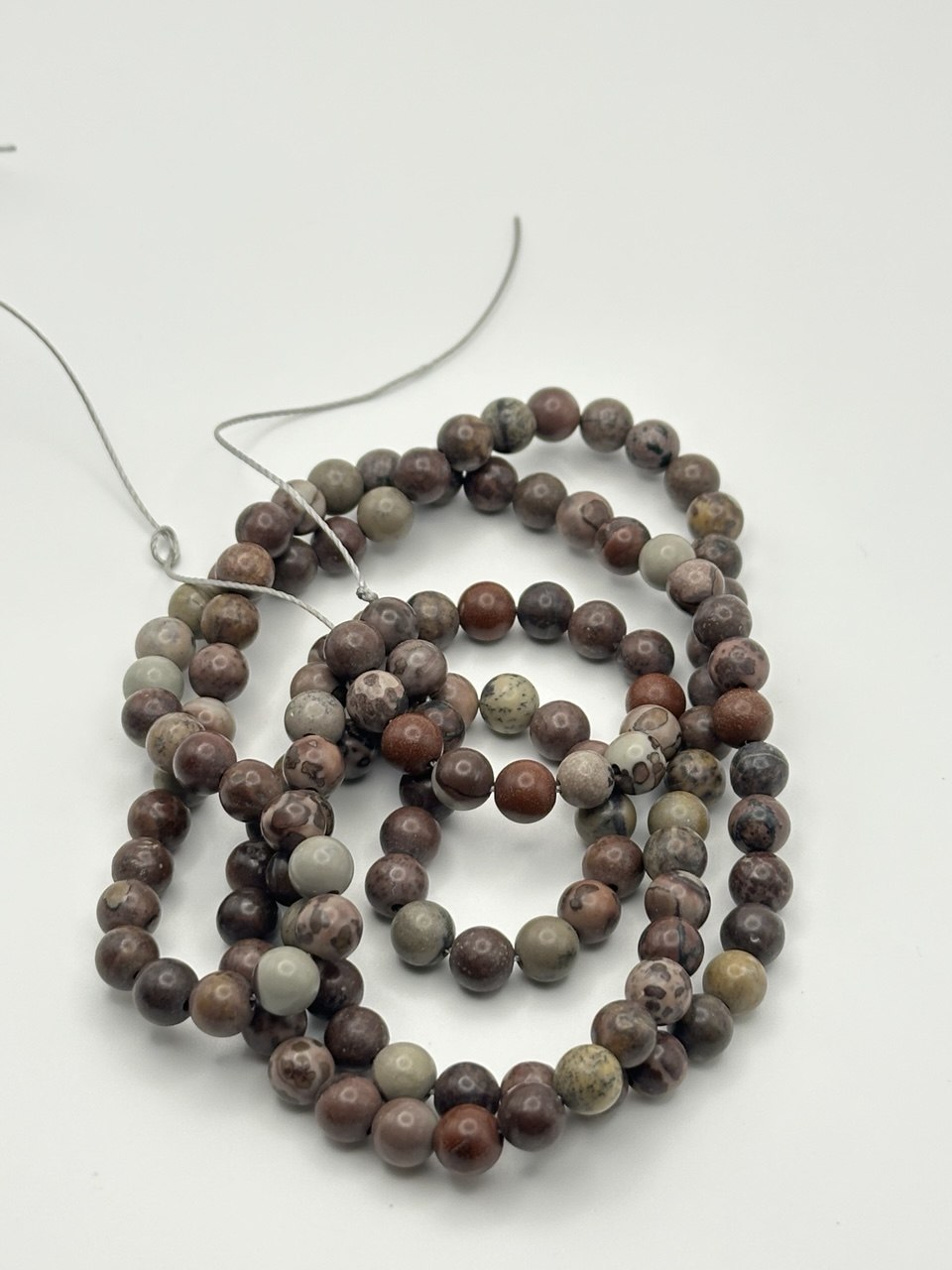 A string of greyish, light brown, and black round agate beads on a white surface