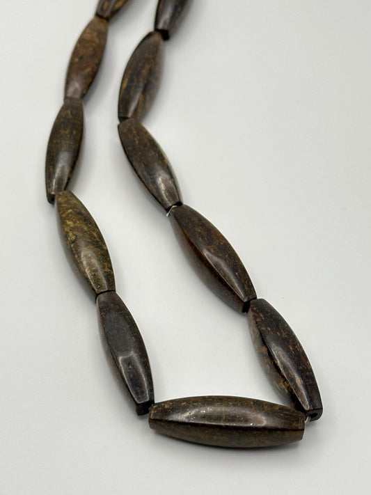 Large puffed bronzite tube shaped beads on a white surface