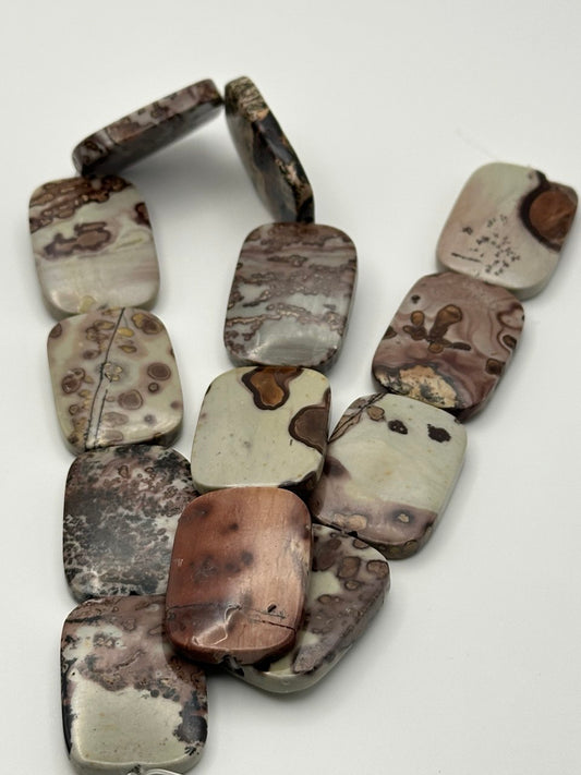 A string of rounded rectangle dendritic jasper beads on a white surface