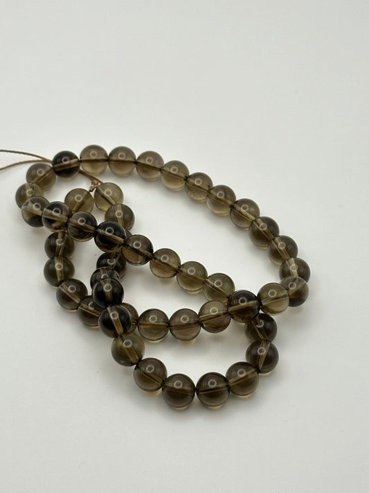 A string of transparent round smoky quartz beads on a white surface