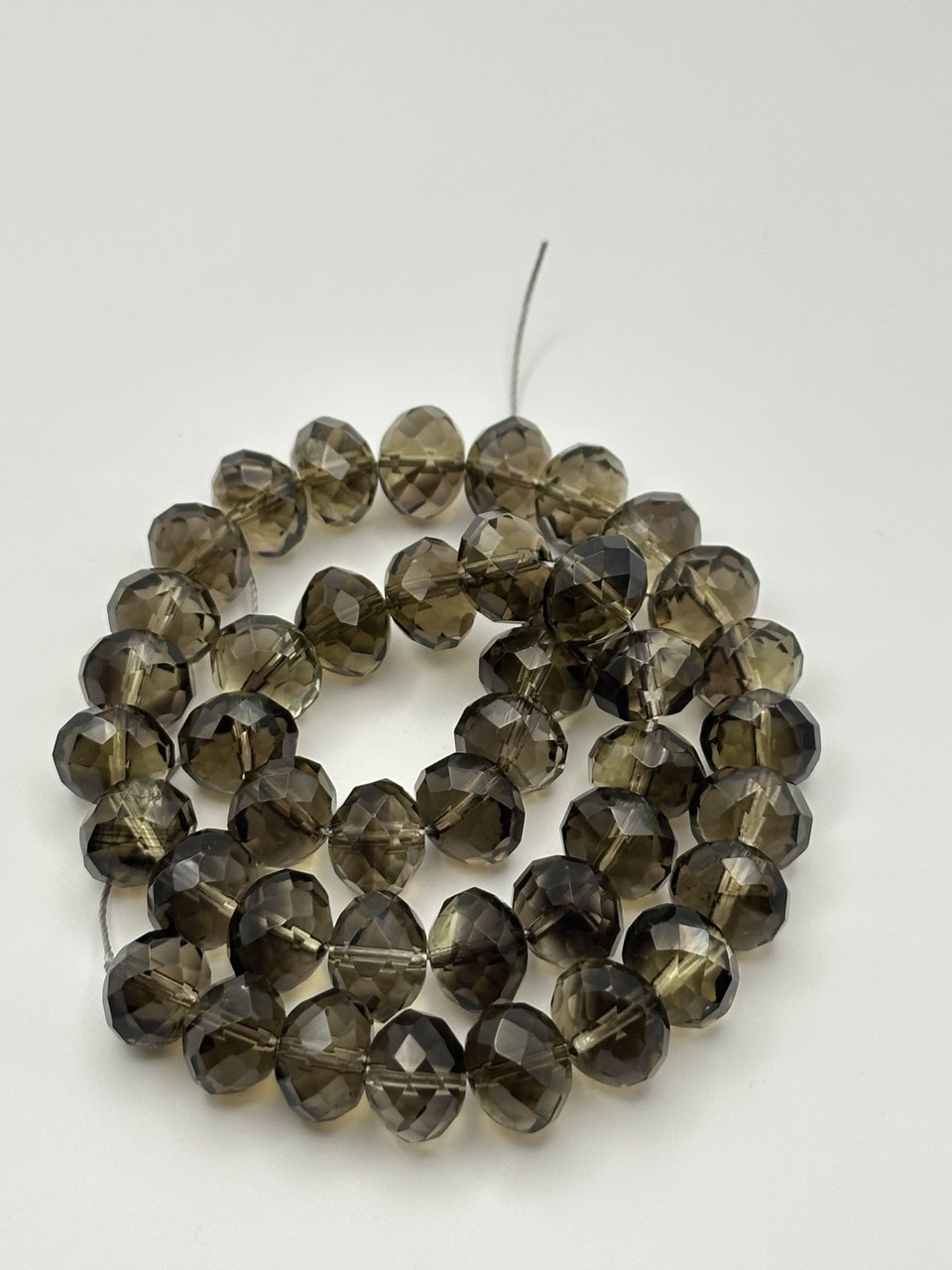 A string of faceted rondelle smoky quartz beads on a white surface