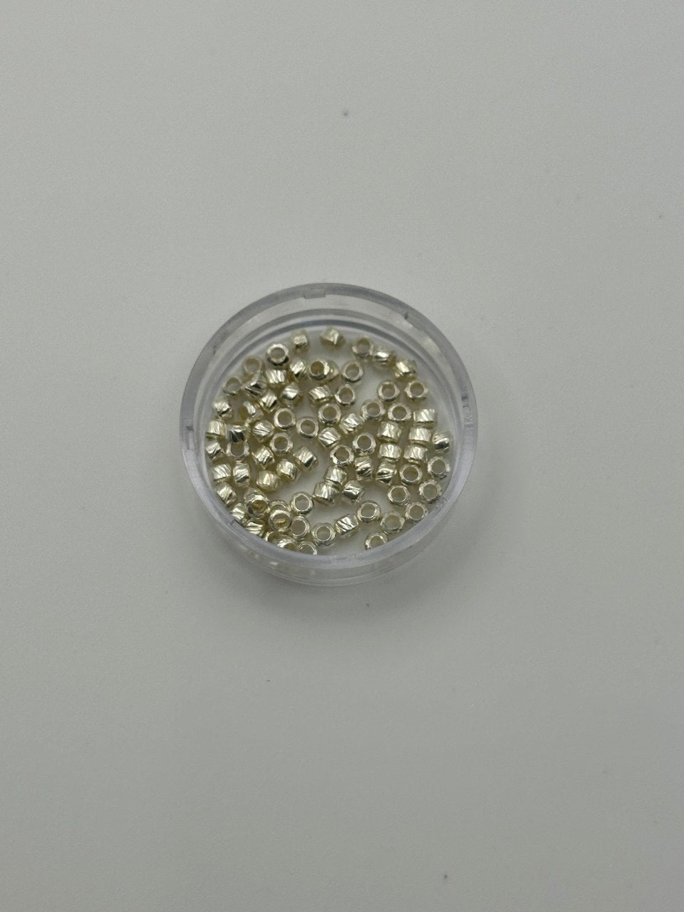 Small container filled with small metallic crimp beads on a gray background