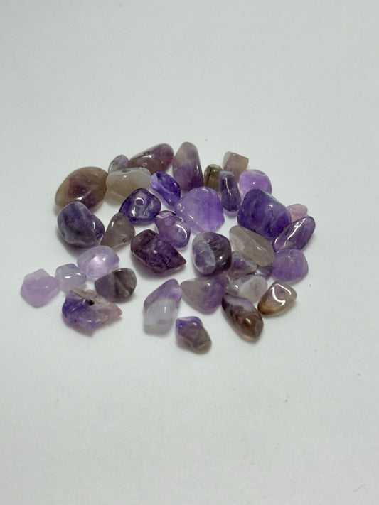 A small pile of polished tumbled purple stones, including amethyst and smoky quartz varieties, arranged on a plain white surface.
