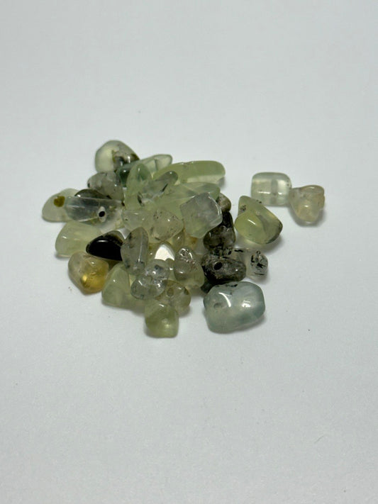 A small pile of polished tumbled gemstones in various translucent shades of green, gray, and clear, arranged on a plain white surface.