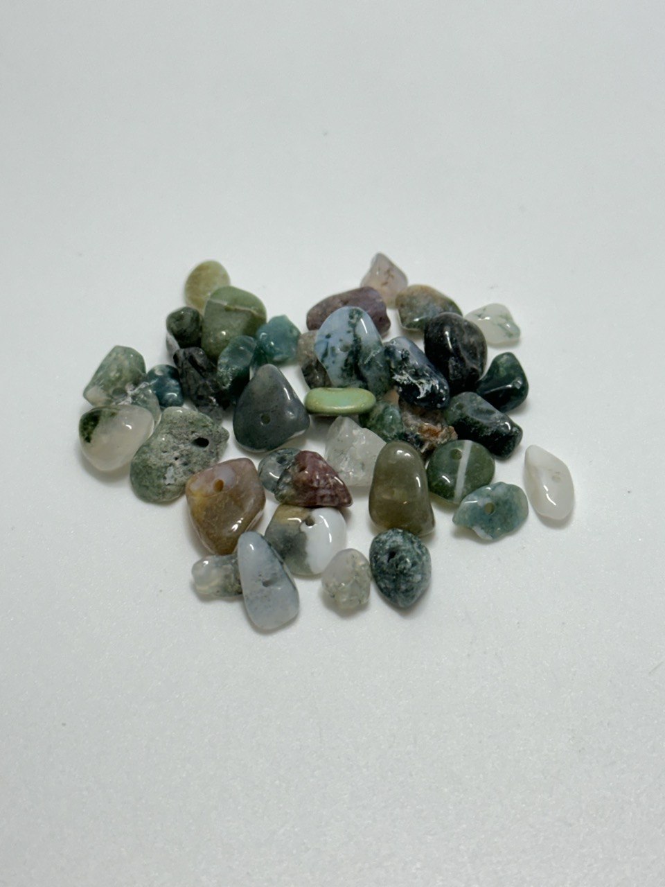 A small pile of green moss agate chip beads on white background