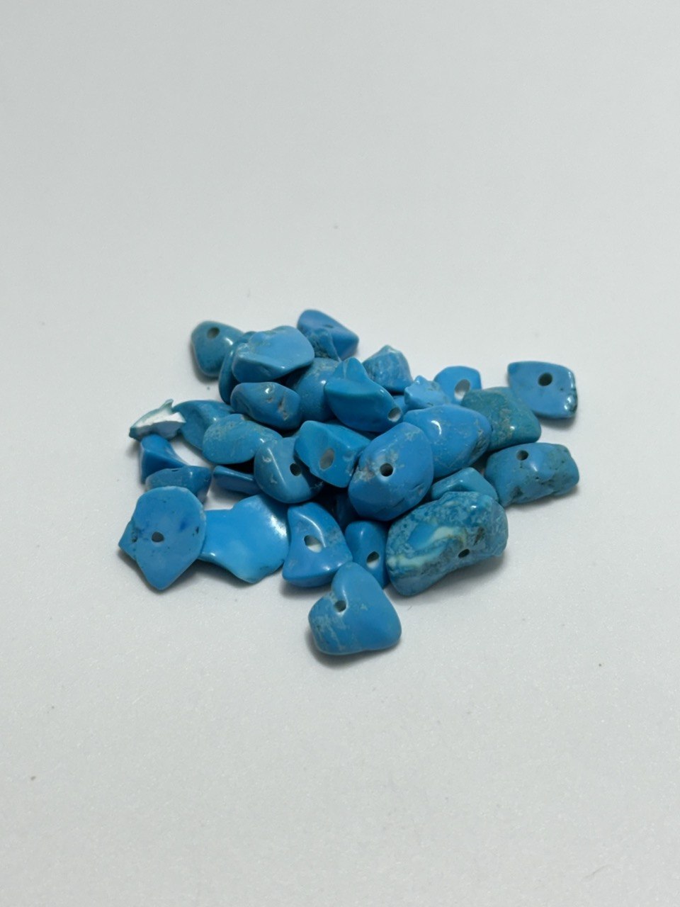 A pile of small, irregular-shaped howlite stones with pre-drilled holes, displayed on a plain light gray background.