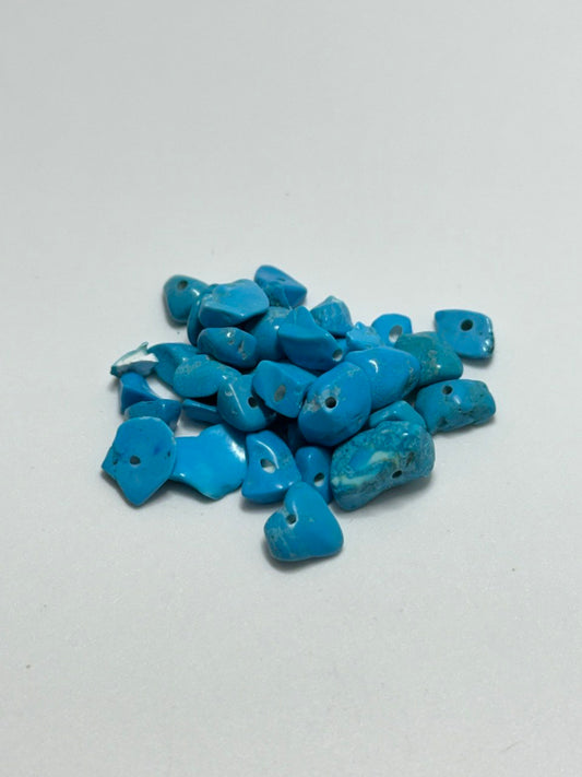 A pile of small, irregular-shaped howlite stones with pre-drilled holes, displayed on a plain light gray background.
