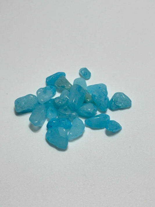 A small pile of tumbled blue quartz chips or pebbles on a plain light gray background.