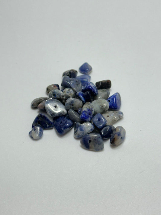 A small pile of polished blue and white tumbled gemstone beads with small holes, arranged on a plain light gray background.