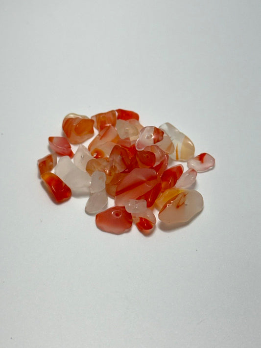 A small pile of polished tumbled carnelian stone chips in shades of orange, red, and translucent white, arranged on a plain light background.