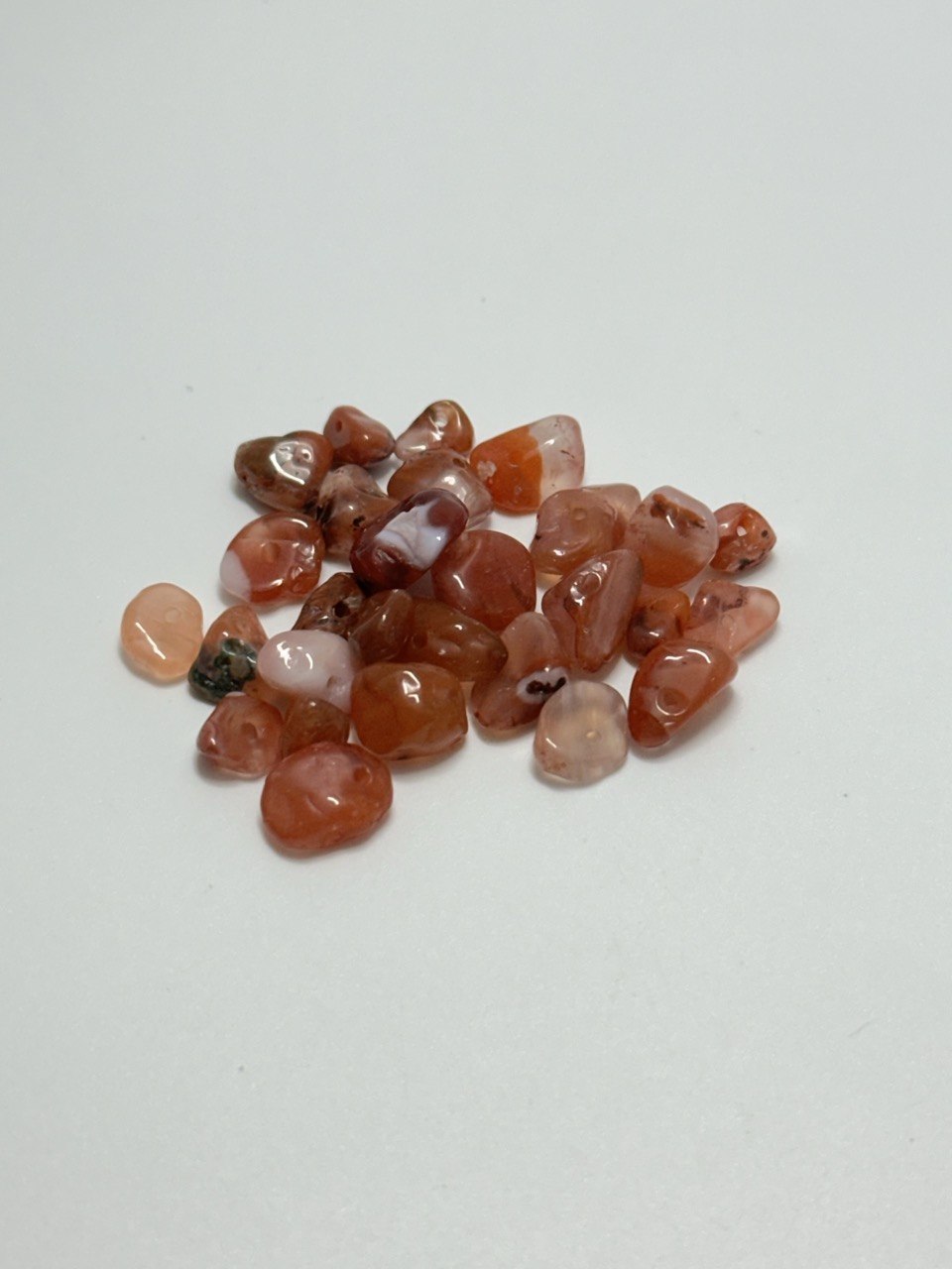A small pile of carnelian agate chip beads on white background