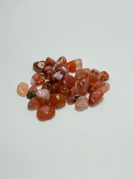 A small pile of carnelian agate chip beads on white background