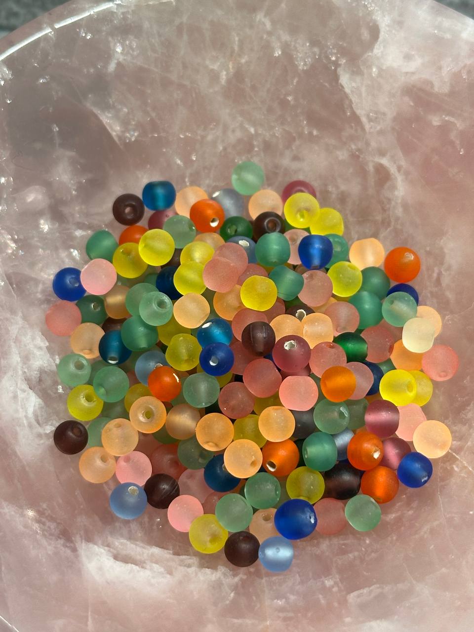 Colorful beads in a clear container on a textured surface
