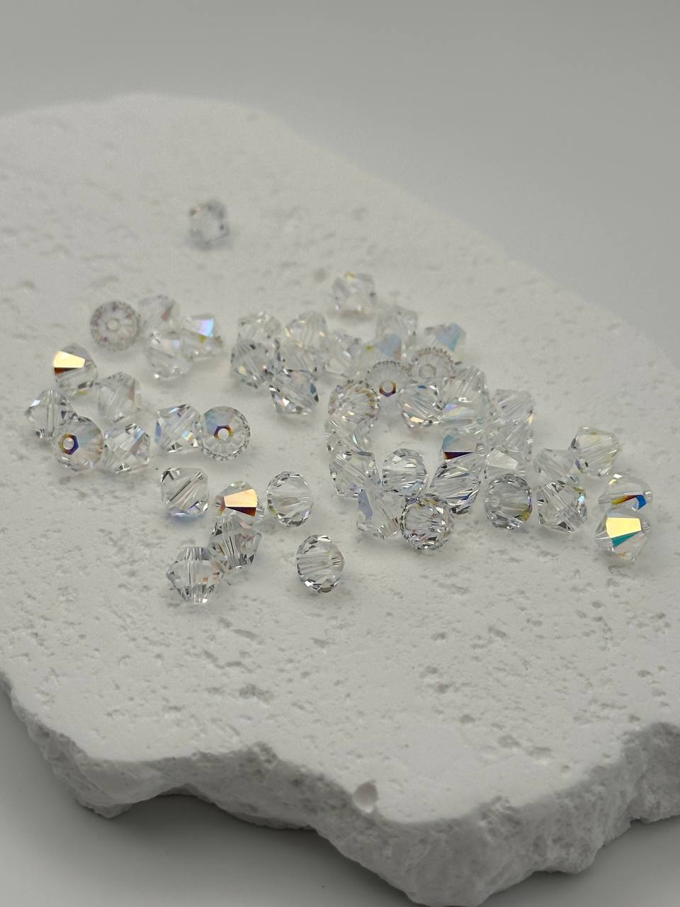 Clear crystal AB bicone beads on a textured white surface