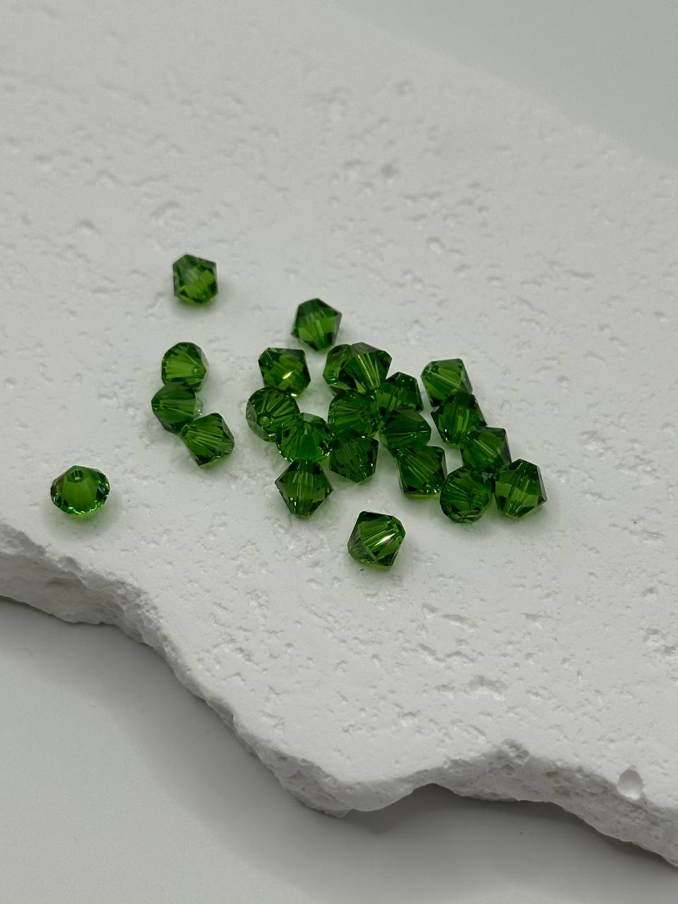 Green crystal bicone beads on a textured white surface