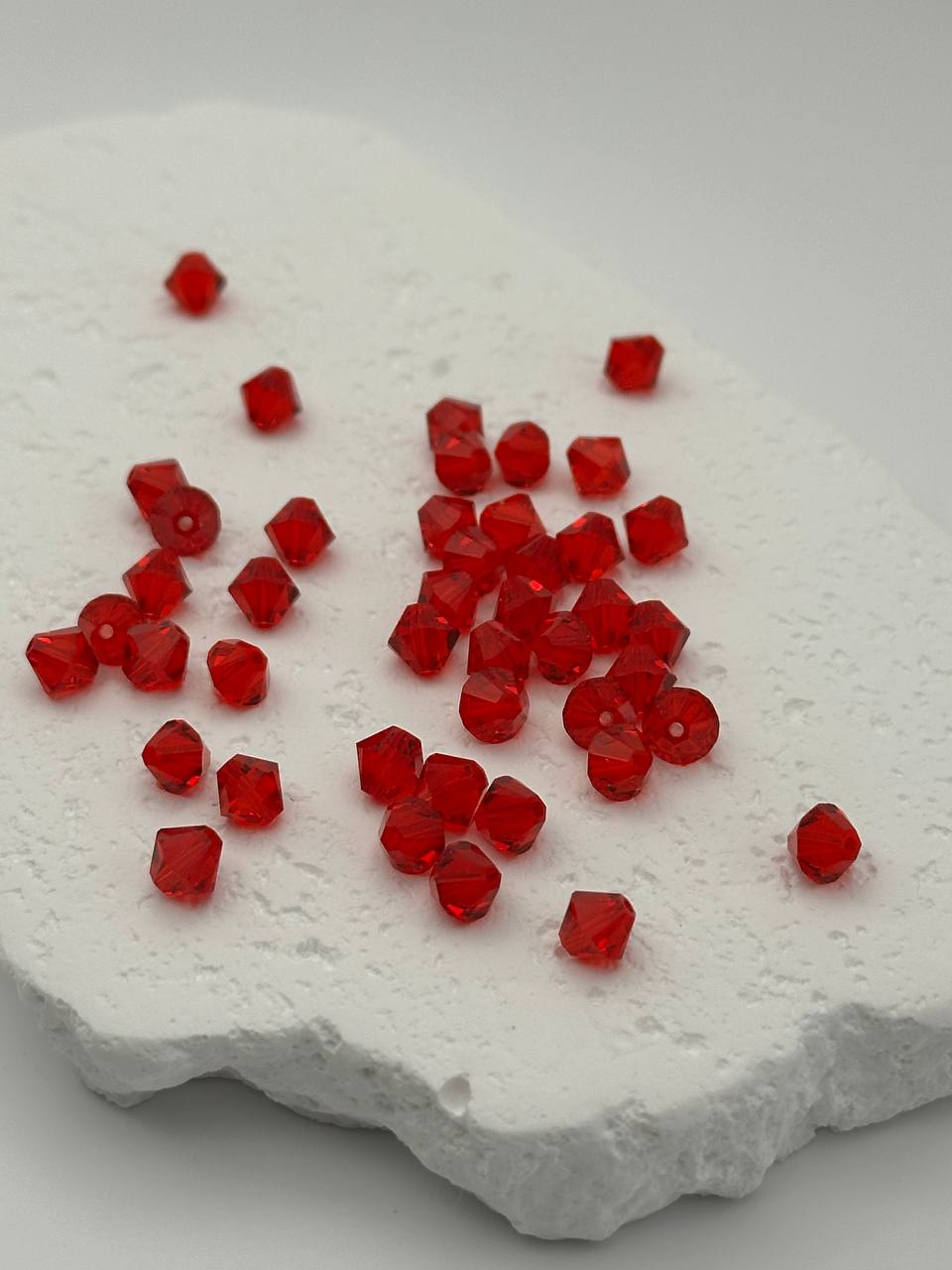 Red bicone beads on a textured white surface
